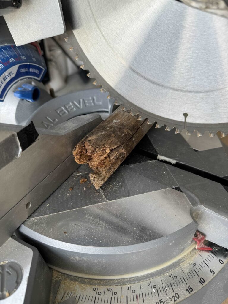 A saw cutting a rotten end off a wood stake. 