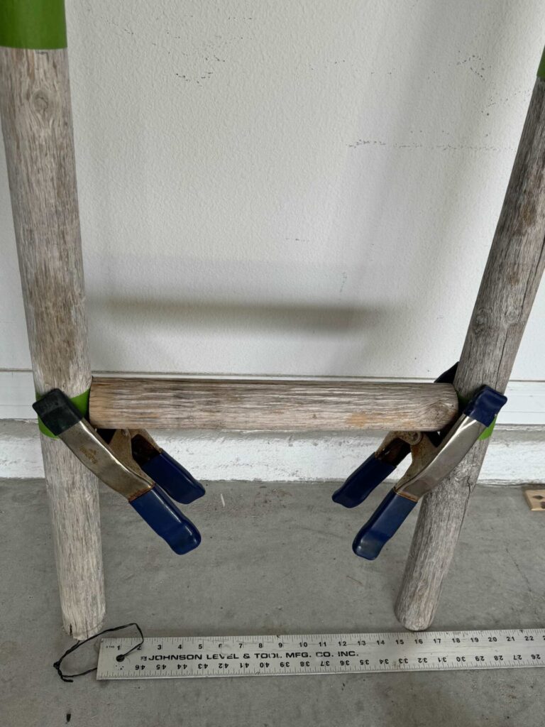 Clamps holding a wooden rung to the side rails of a DIY towel ladder.