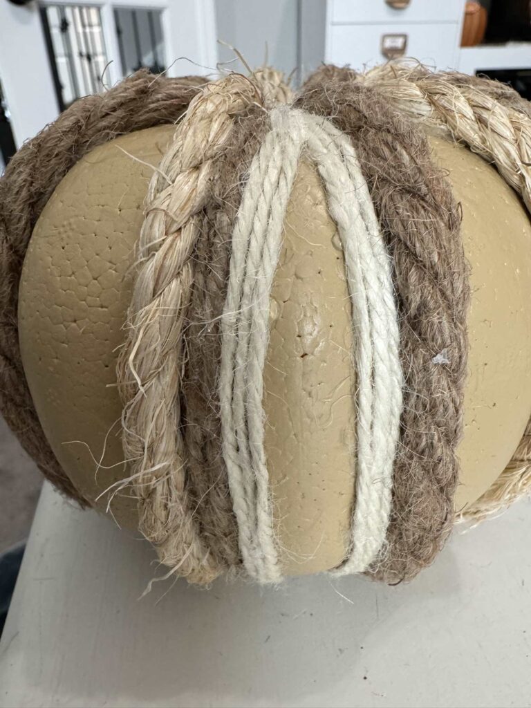 A pumpkin with rope ant twine wrapped around it. 