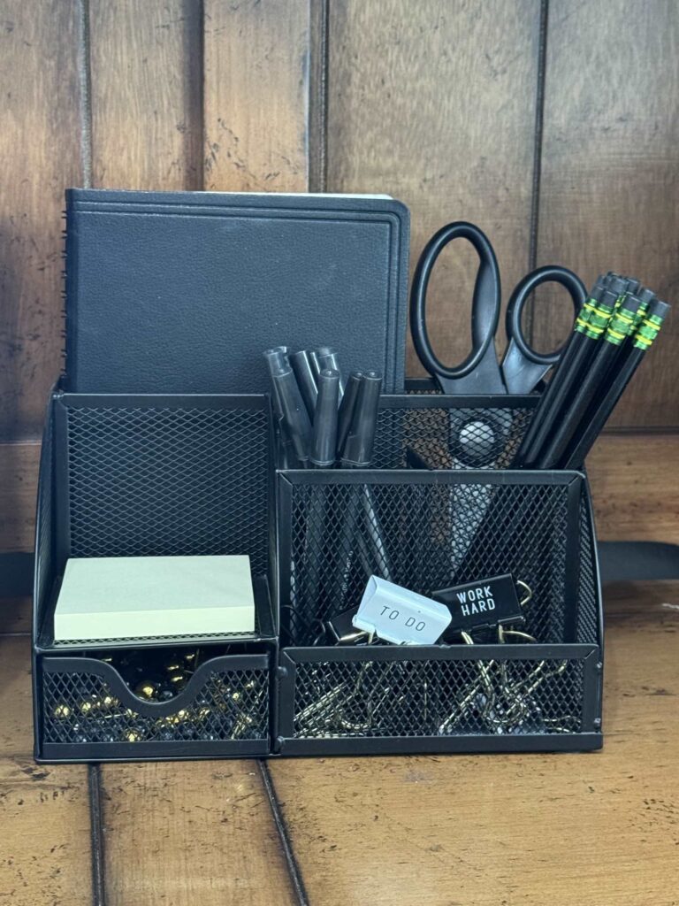 Black desk organizer filled with pens, pencils, clips, post it notes, and scissors ready for back to school..