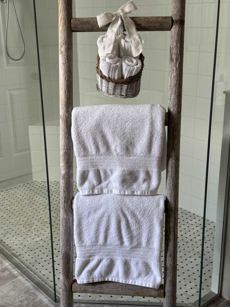 An antique looking towel ladder with 2 white towels and a basket of wash clothes. 