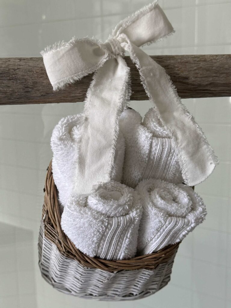 A basket holding white wash clothes with a white ribbon. 