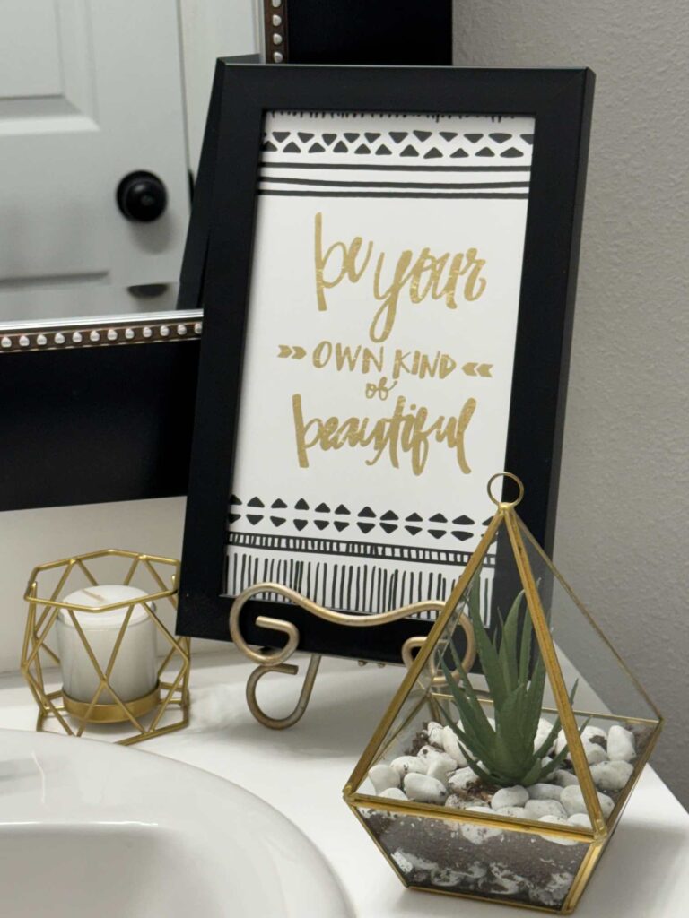 A picture, candle, and succulent decorate a bathroom counter. 