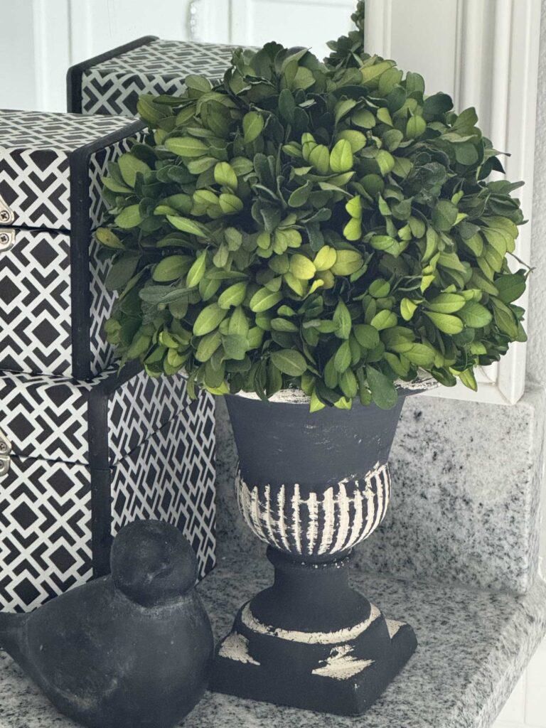 A topiary in a black vase and a black bird sculpture. 