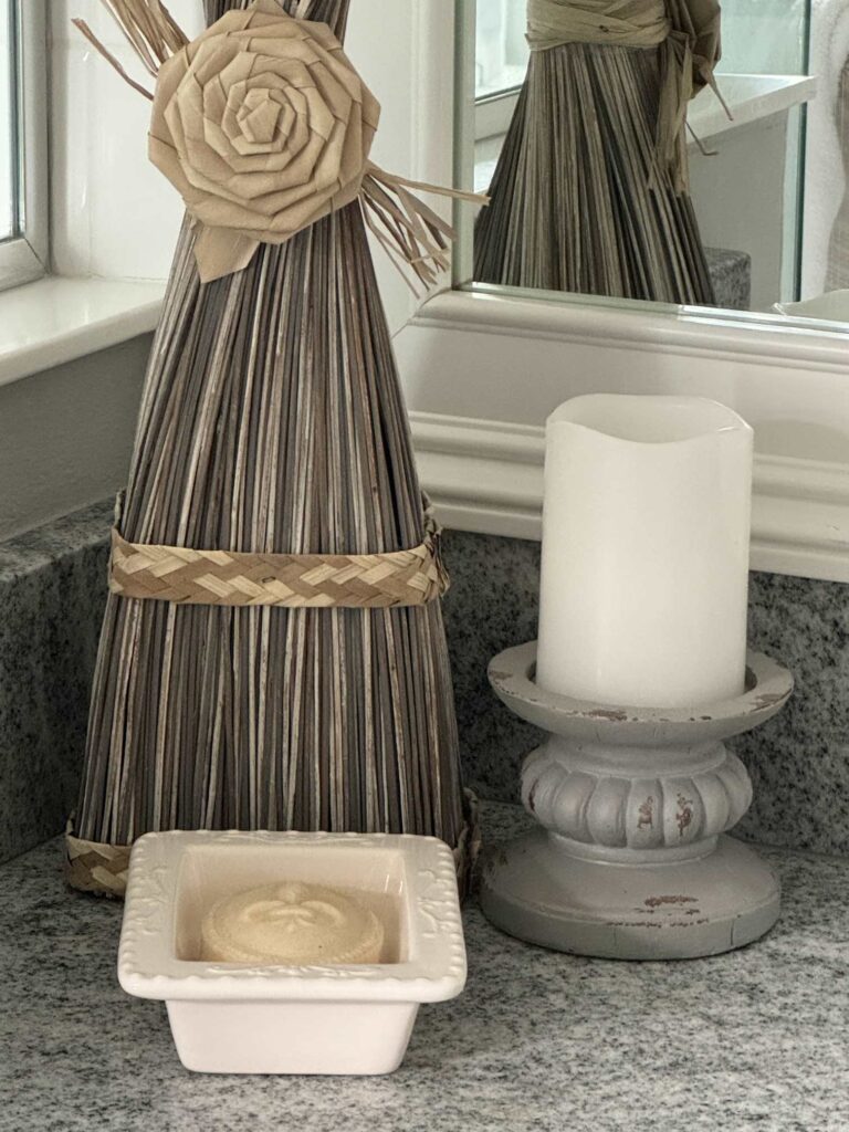 A gray candle holder with white candle and a decorative soap dish sit on a bathroom counter. 