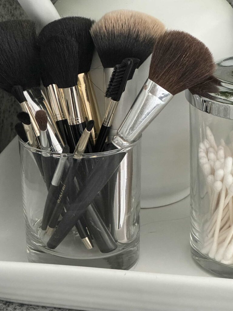 A glass cup holding make-up brushes. 