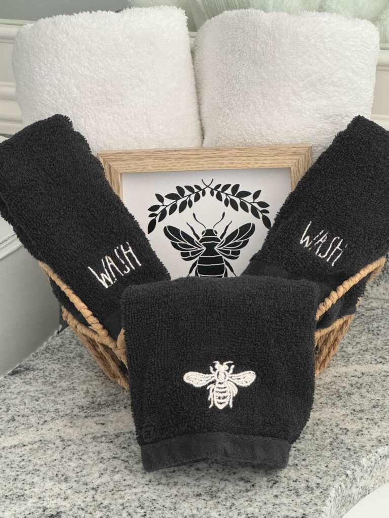 A basket filled with rolled white towels, black washcloths, and a bee picture. 