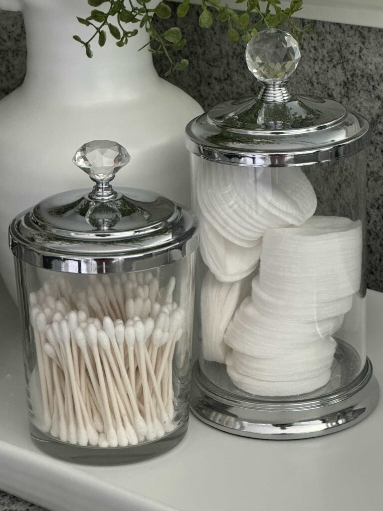 Glass canisters with lids storing cotton swabs and pads. 