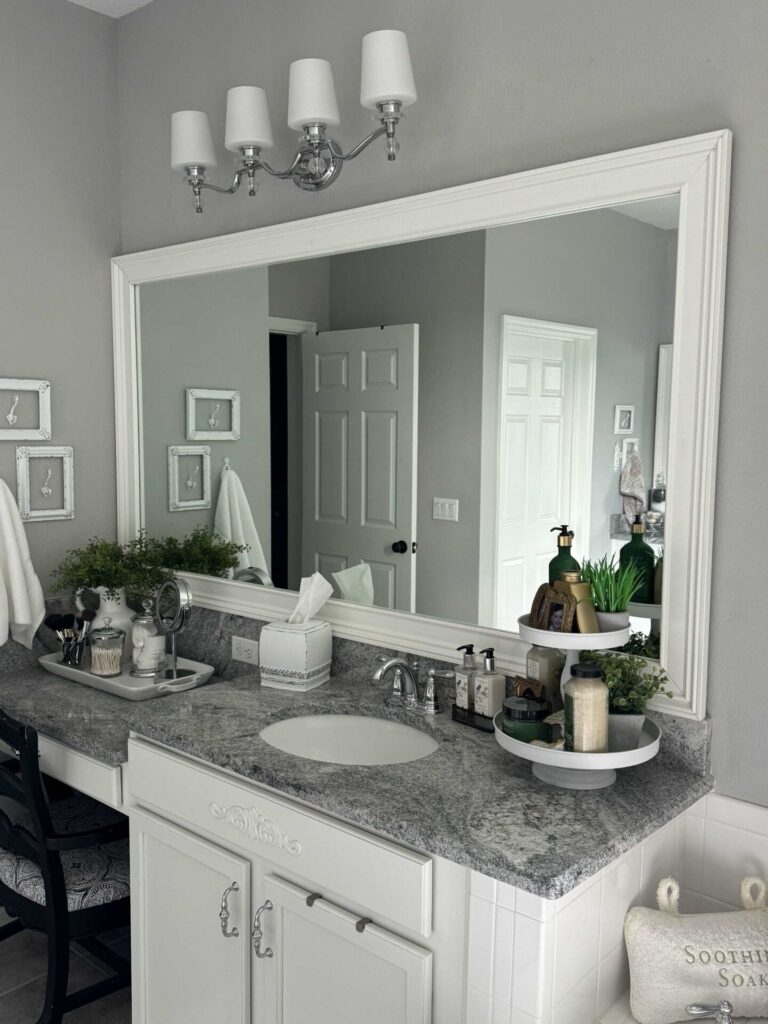 White bathroom cabinet with a white framed mirror over it. 