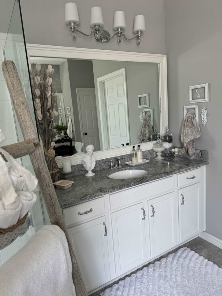 White bathroom cabinet with a white framed mirror above it. 