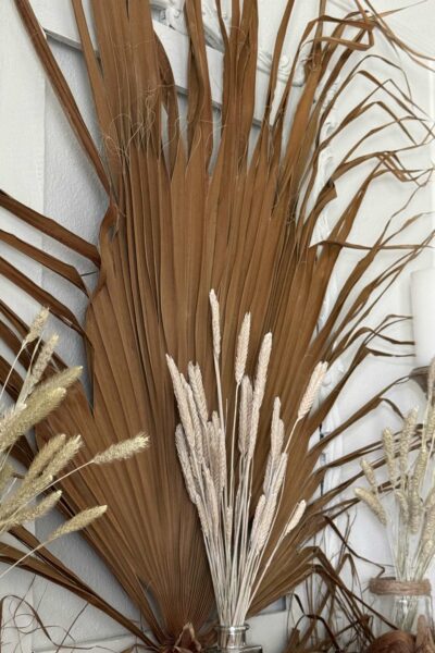 A large dried palm frond and wheat displayed on a mantel.