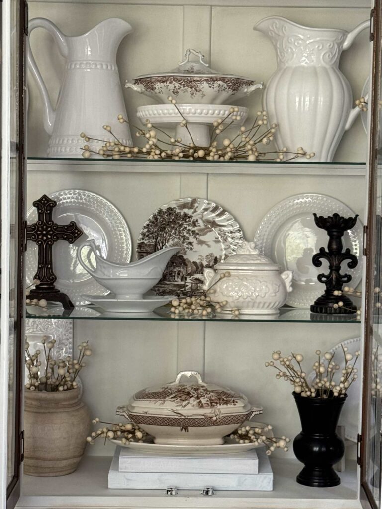 Fall decorating in a China cabinet with white dishes and brown decor. 