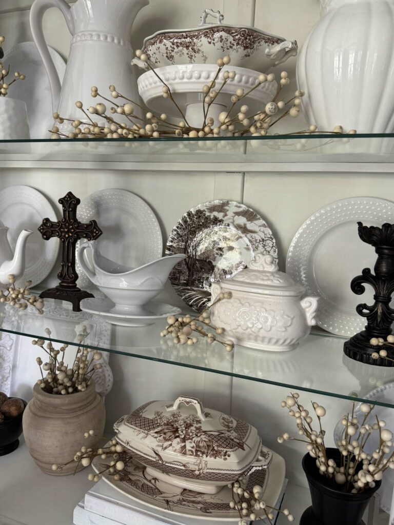 A china cabinet with white dishes and brown decor pieces is an easy fall decorating idea. . 