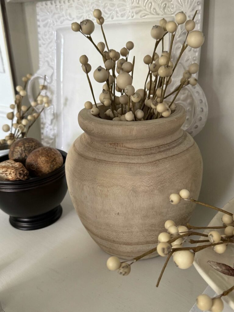 A wood vase filled with neutral faux berries. 