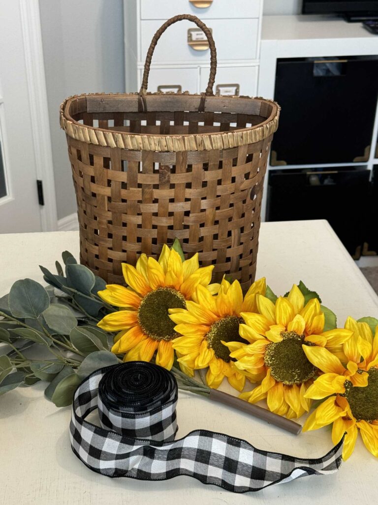 A basket, sunflowers, eucalyptus, and black and white buffalo check ribbon that will be used to make a DIY sunflower wreath.