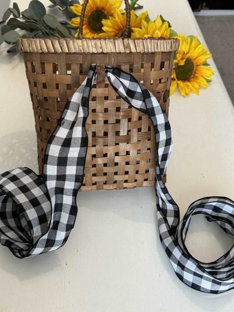 Step one to make a DIY sunflower wreath. is to weave a long piece of black and white buffalo check ribbon through a basket. 