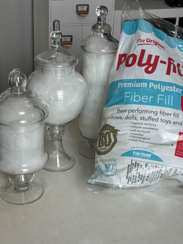 Three apothecary jars filled with fiber fill and a bag of fiber fill beside them. 