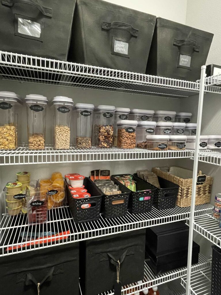 An organized pantry with Oxo containers, black bins and clear bins. 