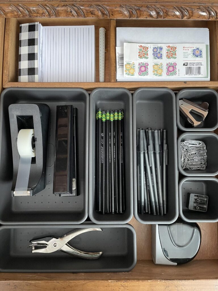 An organized drawer with dividers filled with pens, pencils, tape, and other office supplies. 