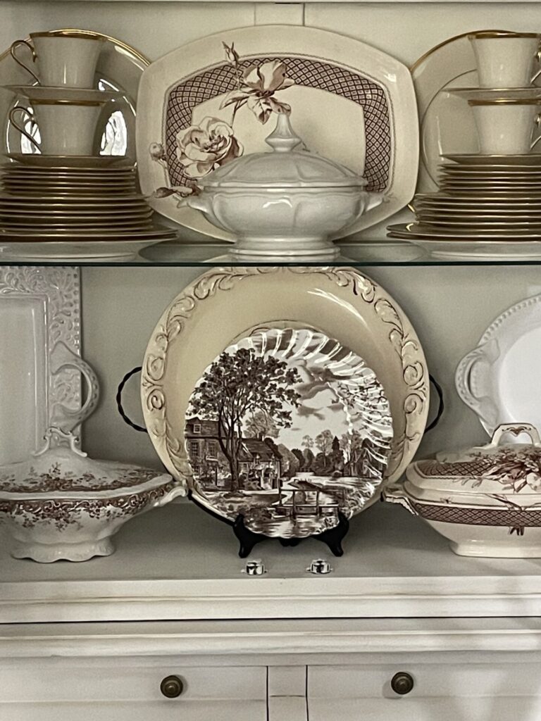 Brown, white, and cream dishes organized in a china cabinet. 