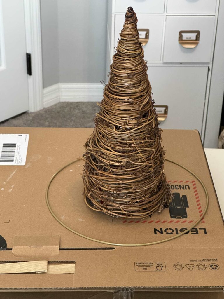 A twine Christmas tree and a metal wreath form sitting on a cardboard box. 