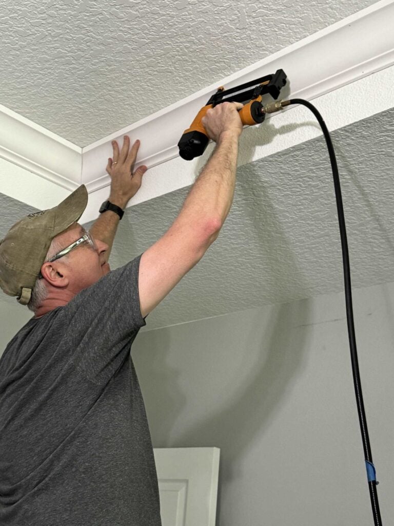 Man nailing crown molding to a ceiling.