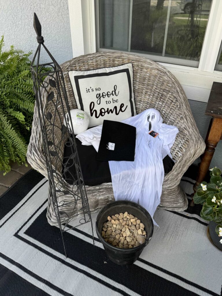 Obelisk, container of rocks, Dollar Tree hanging ghost, black felt, a white sheet, and a styrofoam ball on a front porch. 