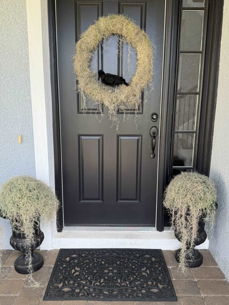 A black front door with a moss wreath and moss covered urns.  