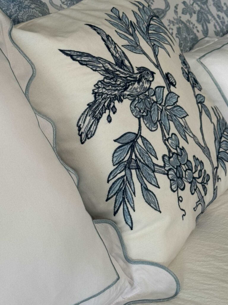 An embroidered pillow with a blue and white bird. 