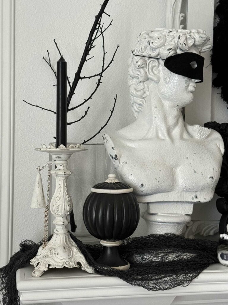 Bust statue with wearing mask next to candle and black pedestal bowl. 