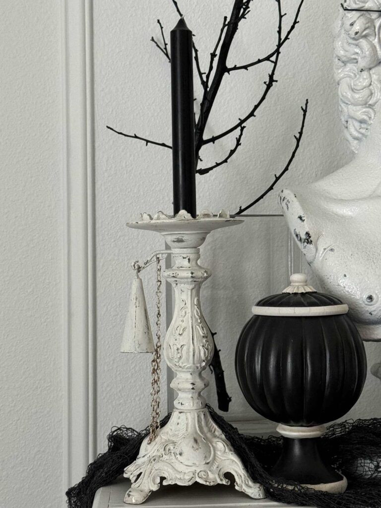 A white vintage candle holder with a black taper candle. 