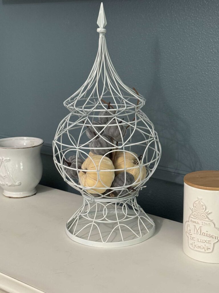 A white metal decorative cage holding velvet pumpkins. 