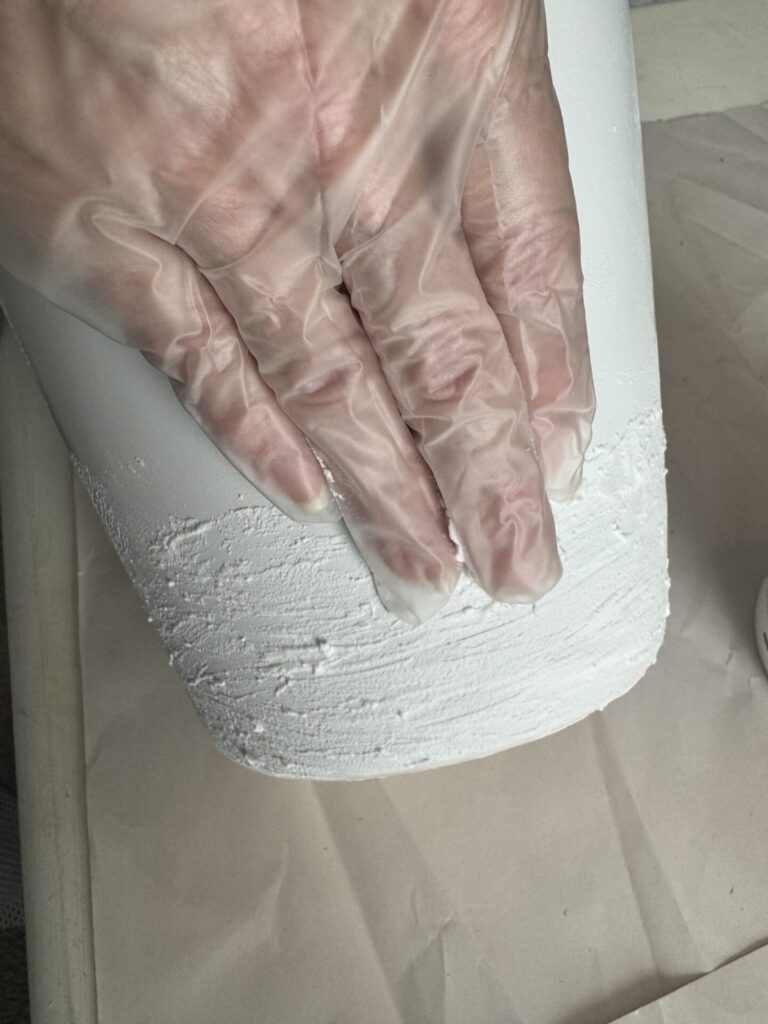 A gloved hand spreading spackling on a vase. 