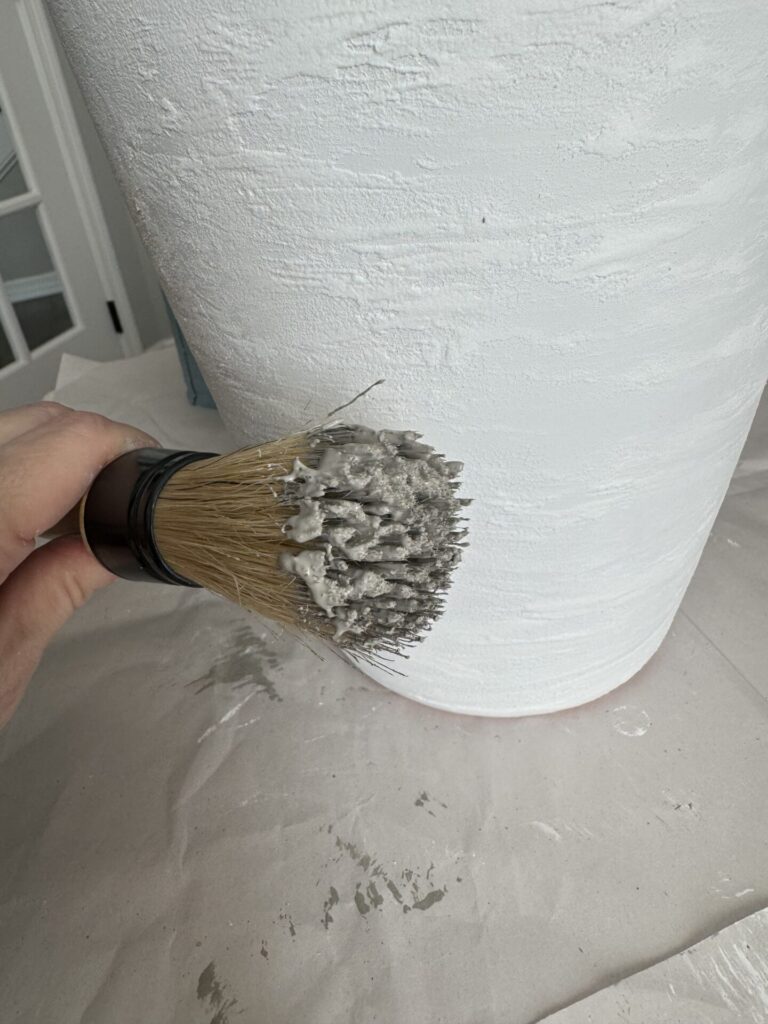 A round paintbrush with gray paint on the end. 