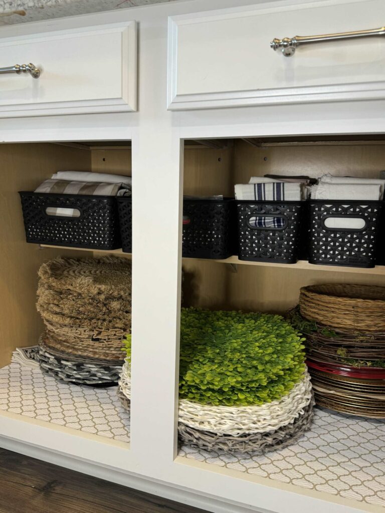 A cabinet with stacked placemats and black bins holding tablecloths and napkins. 