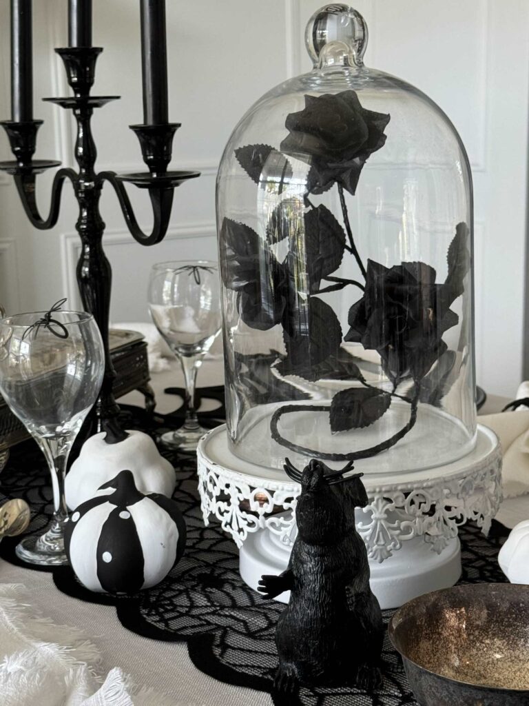 Black roses in a cloche are the centerpiece for a Halloween tablescape. 