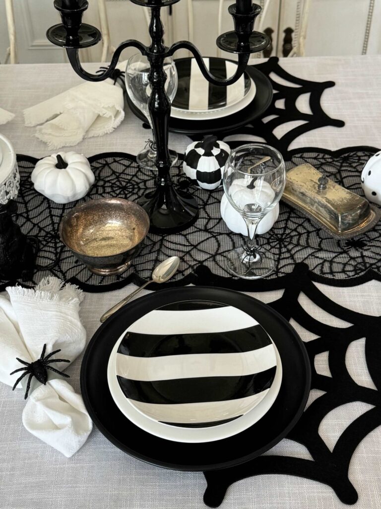 A table setting with spiderweb placemats, black and white dishes, and napkin holders with spiders. 