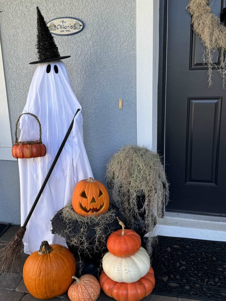 Halloween porch decorated with a ghost witch and orange and white pumpkins. 