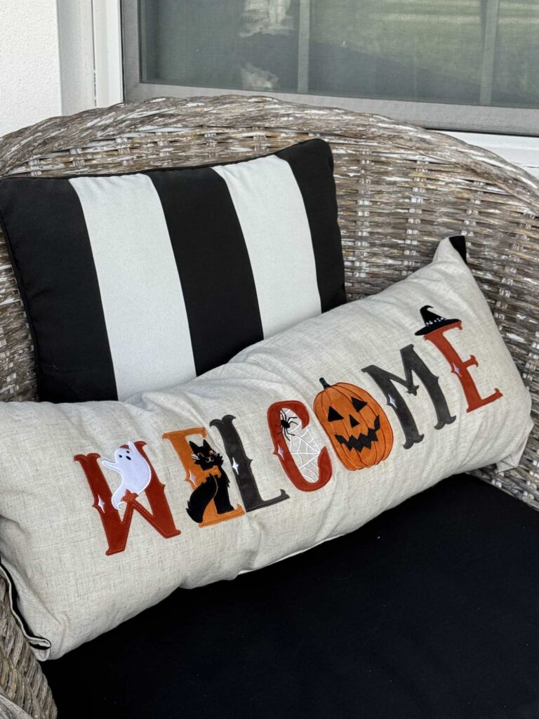 A Halloween welcome pillow sitting in a chair on a front porch. 