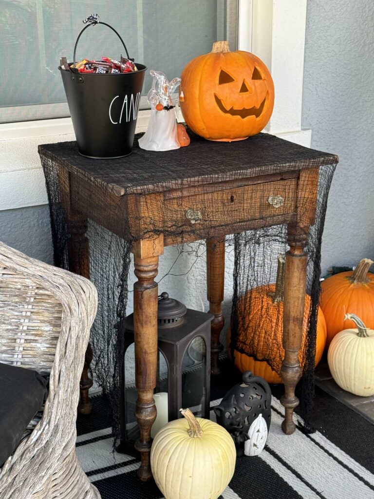 Table on a porch draped with creepy cloth holding Halloween candy. 