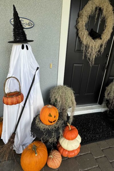 Ghost dressed as a witch surrounded by pumpkins on a porch.