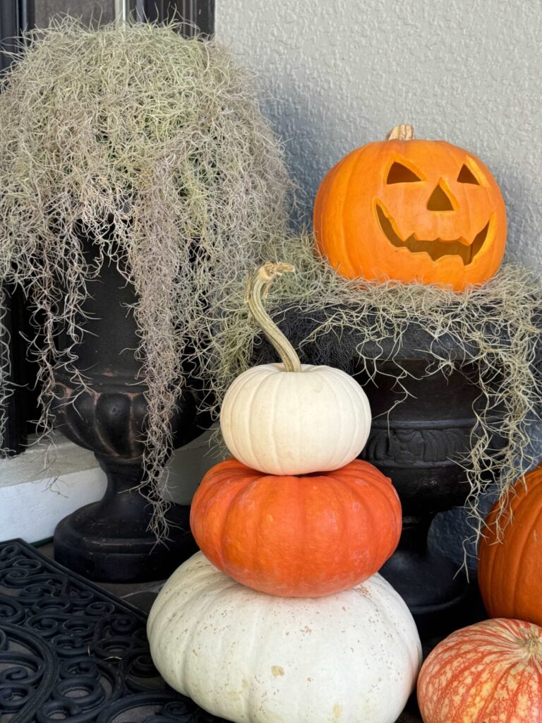 An orange and white pumpkin stack by a jack-o-lantern. 