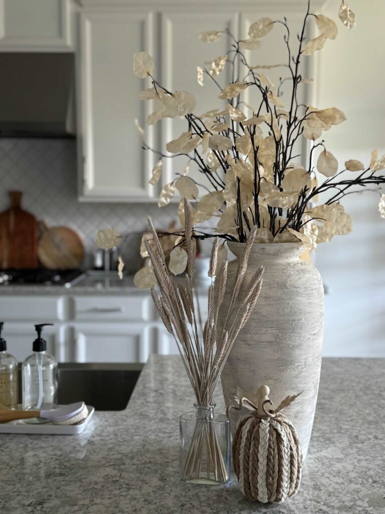 Vase on a kitchen counter filled with neutral stems. 