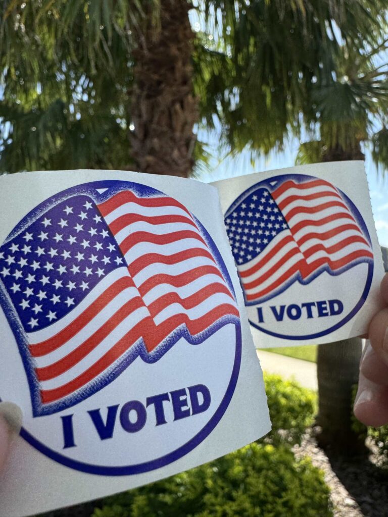 Two people holding up I voted stickers. 