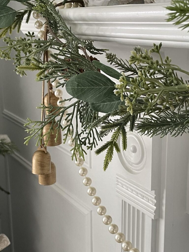 Greenery, bells, and a pearl garland on a Christmas mantel. 