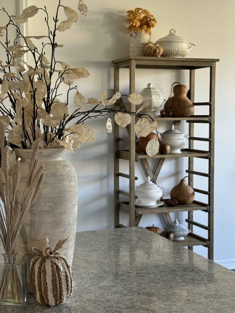 A pie shelf decorated with tureens and gourds for a fall home tour. 