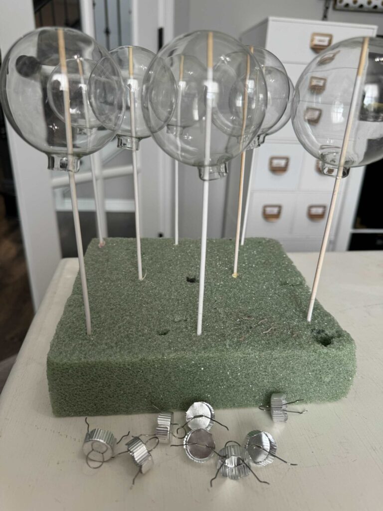 glass ornaments on wooden skewers with their caps laying in front of them. 