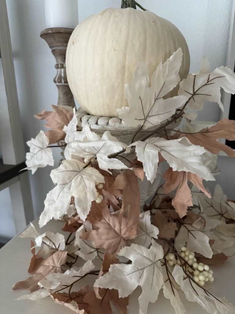 A neutral leaf garland wrapped around an urn holding a white pumpkin. 