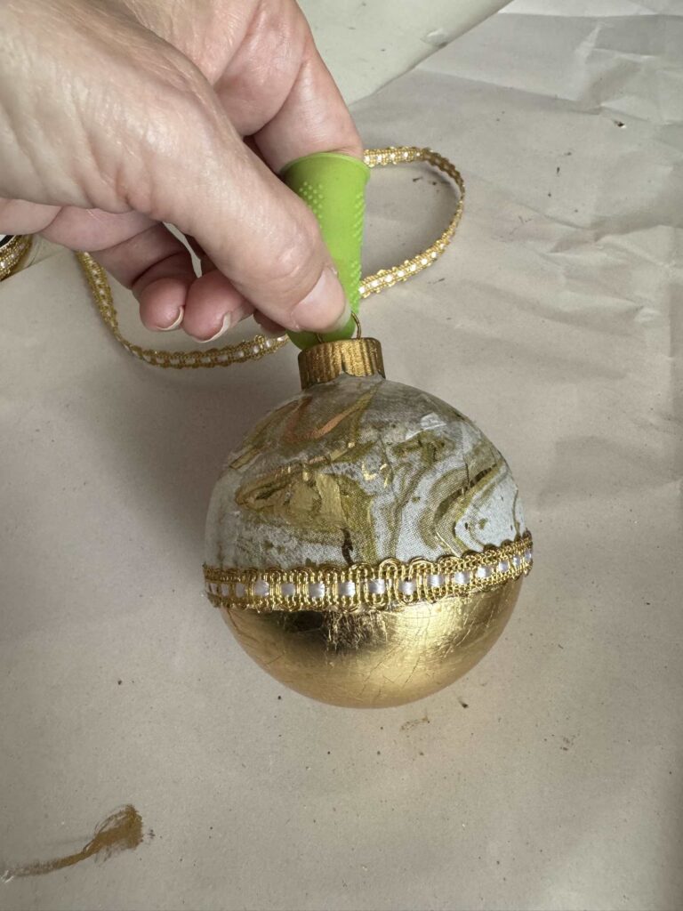 Ornament with half gold leaf and half decoupage with ribbon between it. 