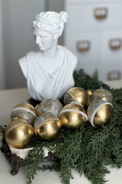 DIY Gold leaf ornaments on a bed of evergreens with statue behind.